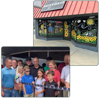Storefront of Boots & Soles featuring large painted sunflowers, a farm scene, swirling sky details, and a figure in overalls on the center window. The artwork covers multiple window panels beneath a red awning.